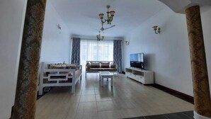 A spacious living room with a sofa set, a TV, and a chandelier. - Stay.Plus Queen's Royal Apartments Nyali (Mombasa)