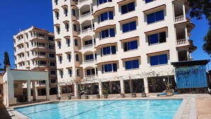 A swimming pool with a building in the background. - Stay.Plus Queen's Royal Apartments Nyali (Mombasa)