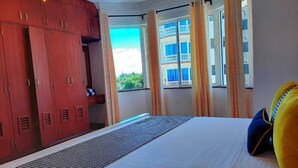 A hotel room with a bed, a wardrobe, and a window with curtains. - Stay.Plus Queen's Royal Apartments Nyali (Mombasa)