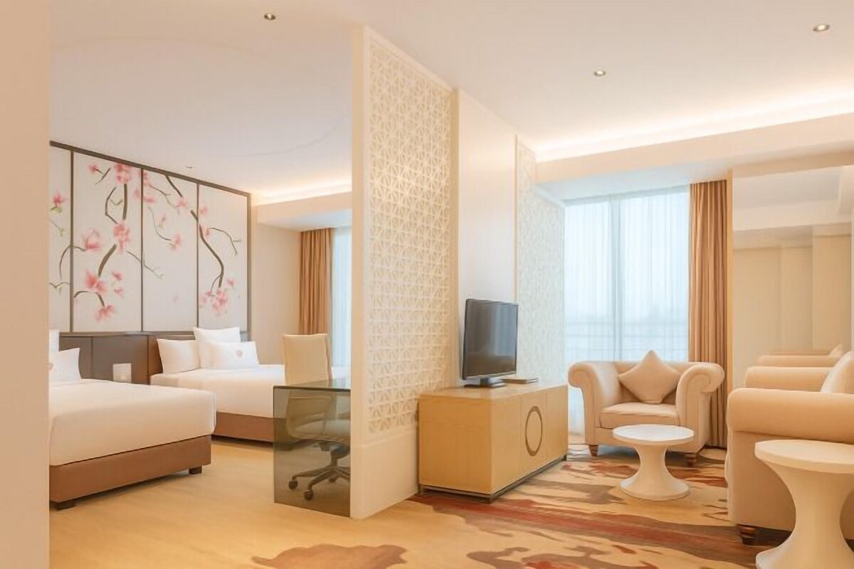 A hotel room with two beds, a TV, a seating area with a sofa and armchairs, and a decorative wall with floral artwork.