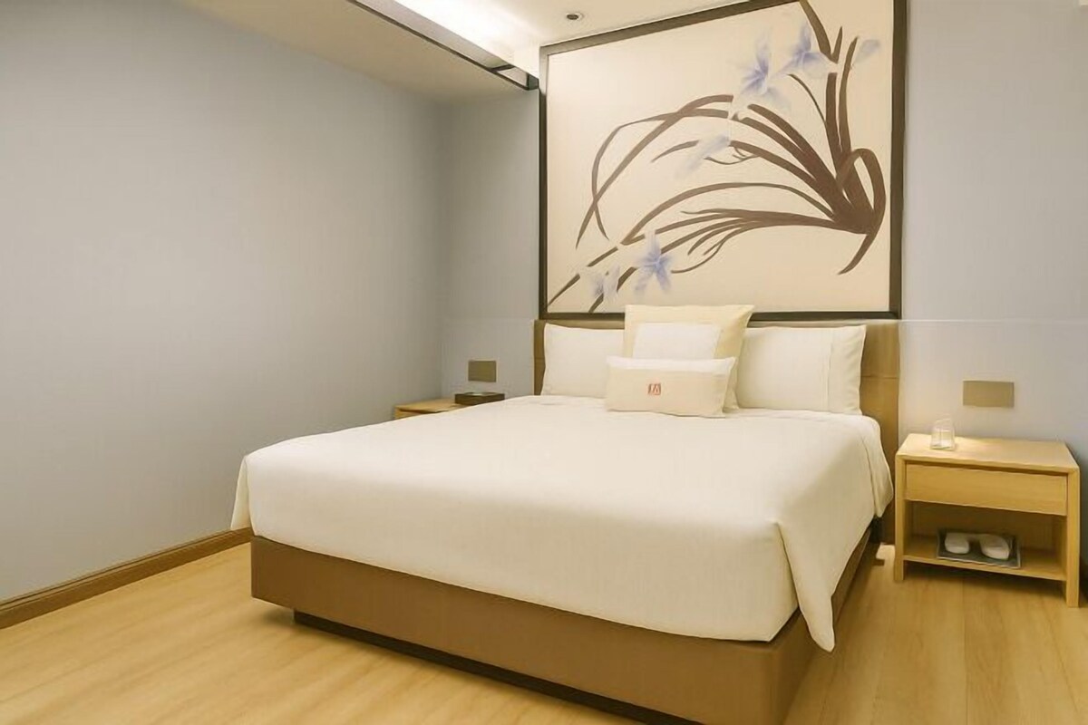 A neatly arranged hotel room with a large bed, bedside tables, and a wall-mounted artwork.