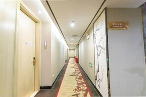 Un corridoio d'albergo con pavimento rivestito di moquette, porte a sinistra e un muro con un cartello a destra.