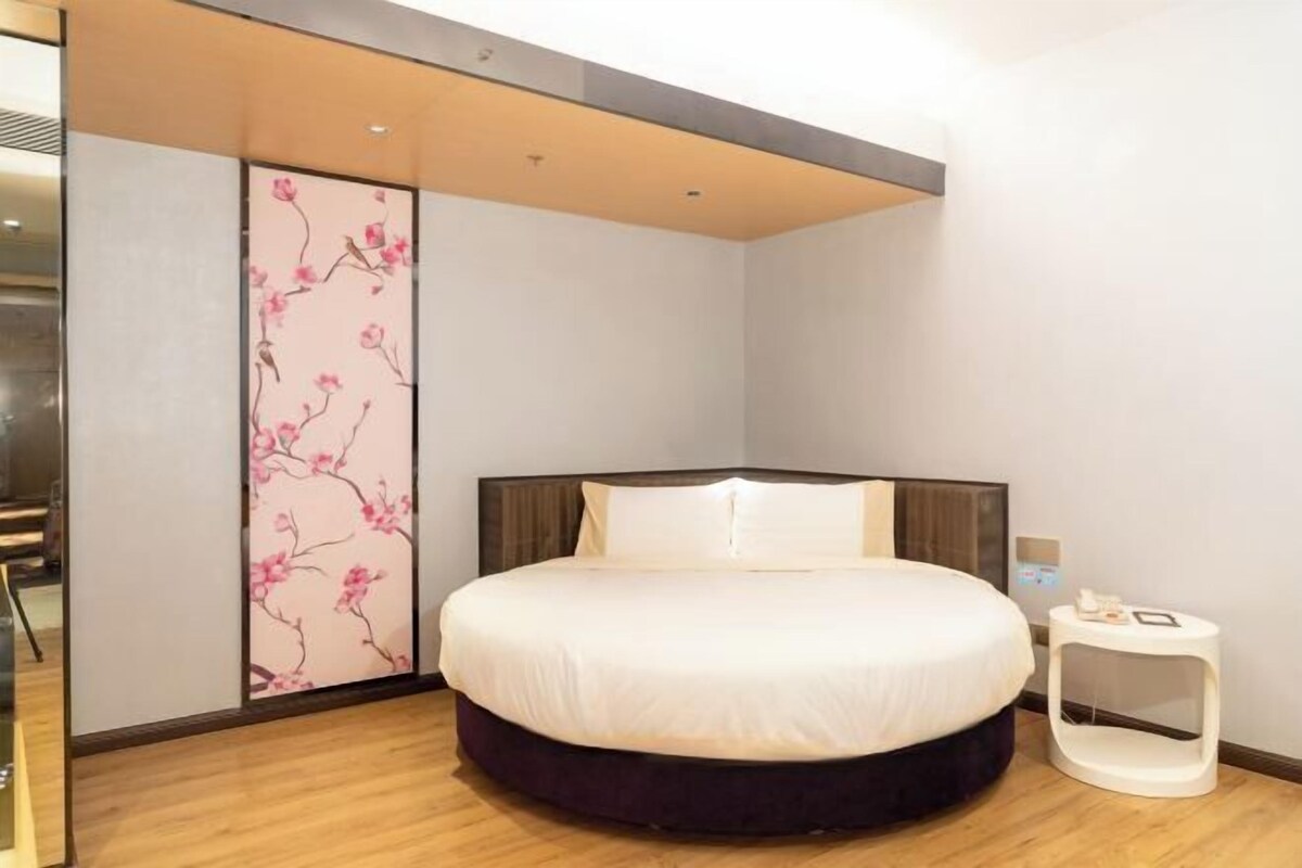 A modern bedroom with a large bed, a wooden floor, a sliding door with floral design, and a small bedside table.