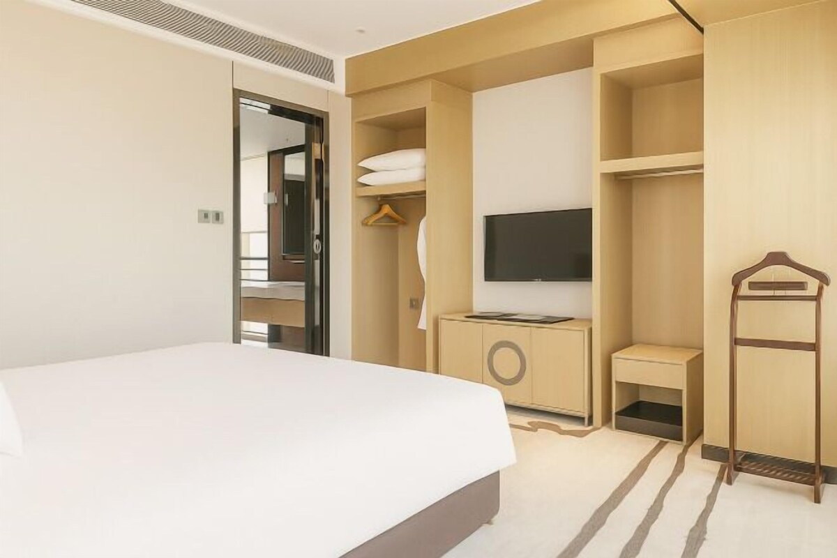 A hotel room with a bed, a TV, a wardrobe, and a small table.