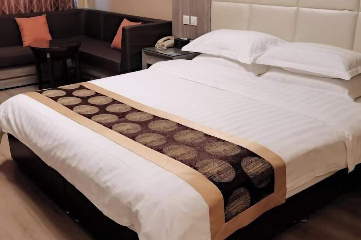 A hotel room with a large bed, a sofa, a small table, and a nightstand with a telephone.