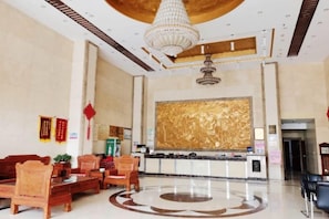 Un vestíbulo de hotel con mostrador de recepción, zona de estar y un gran elemento decorativo en la pared.