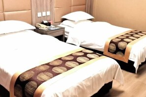 A hotel room with two beds, each with a white duvet and a patterned bedspread. There is a nightstand with a telephone and a lamp between the beds. - Fuhua Hotel (Shouguang)