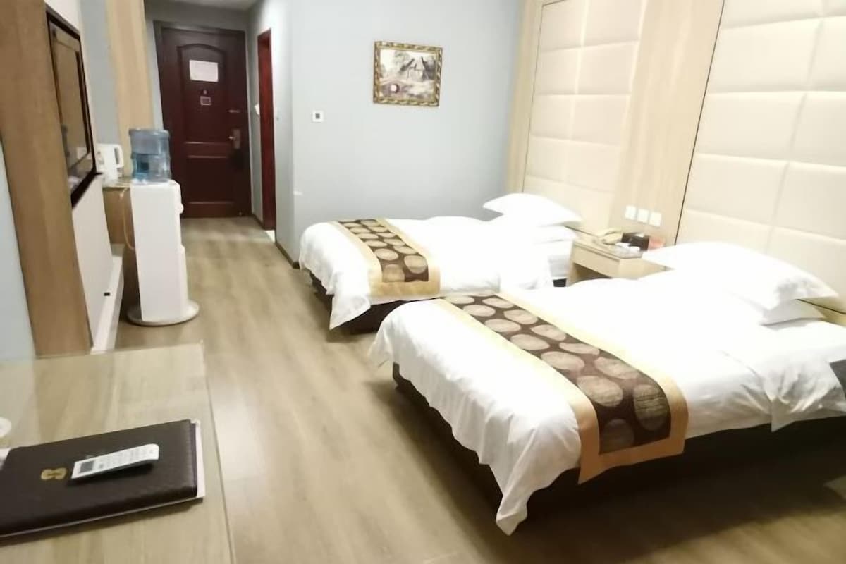 A hotel room with two beds, a desk, a water dispenser, and a door.