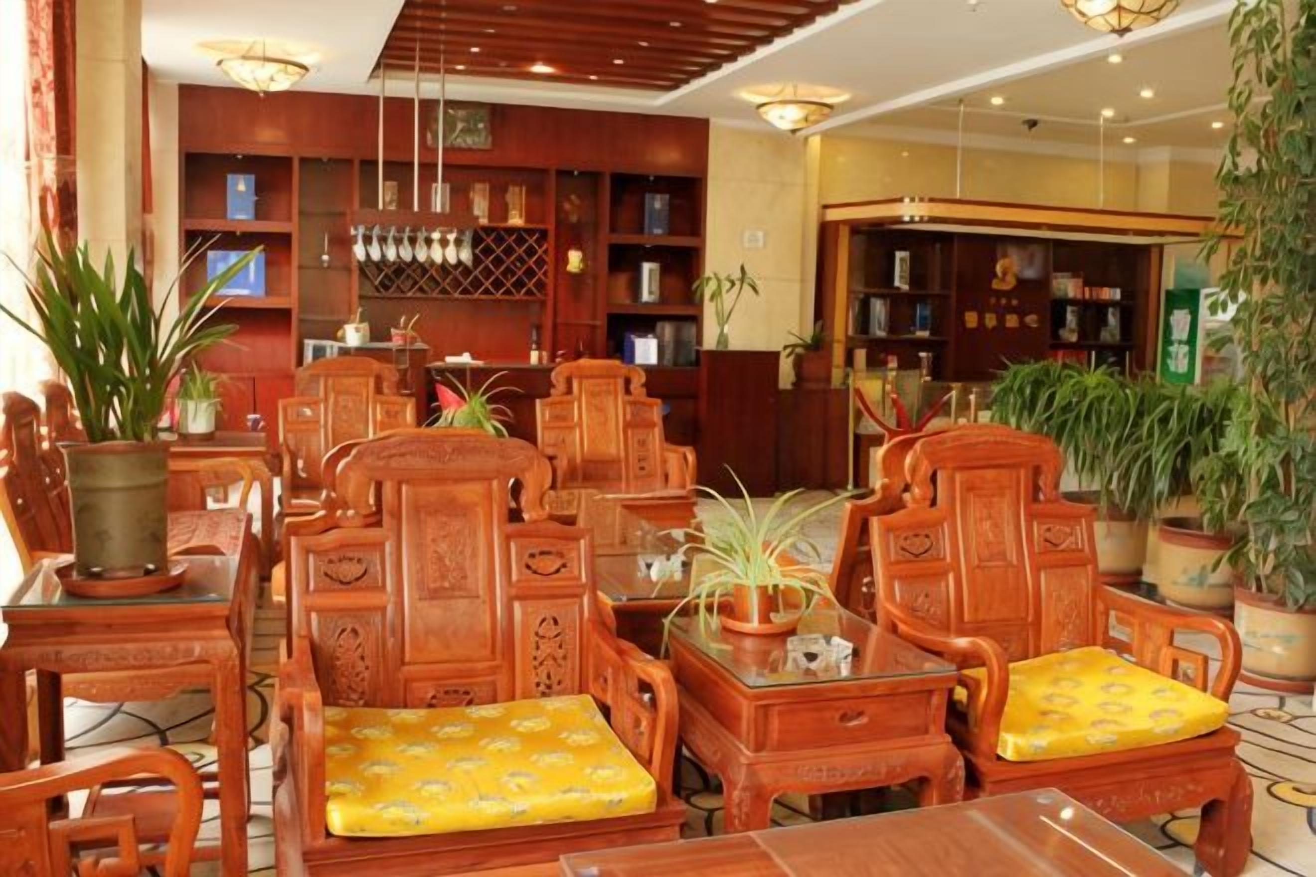 A traditional wooden furniture arrangement with chairs and tables, surrounded by bookshelves and potted plants.