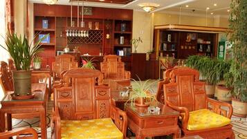 A traditional wooden furniture arrangement with chairs and tables, surrounded by bookshelves and potted plants.