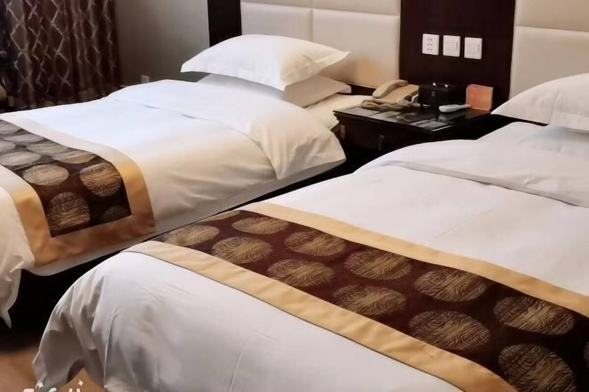 A hotel room with two beds, each with white bedding and a patterned bedspread. There is a nightstand with a phone and a lamp.