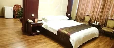 Een hotelkamer met een houten vloer, een bed met een witte dekbedovertrek, een nachtkastje met een telefoon, een stoel en een klein tafeltje met een vaas.