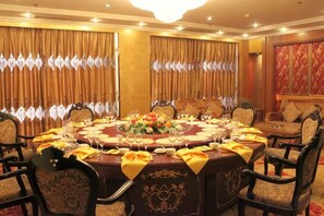 Una mesa redonda dispuesta para comer, rodeada de sillas, en una habitación con cortinas y un papel tapiz estampado.