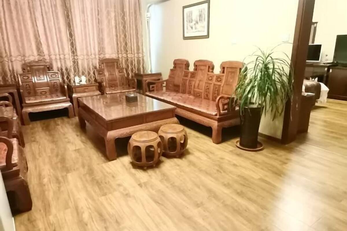 A traditional wooden furniture set including a sofa, coffee table, and stools, with a potted plant and a television in the background.