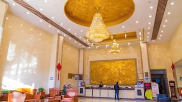 A hotel lobby with a reception desk, seating area, and a chandelier.