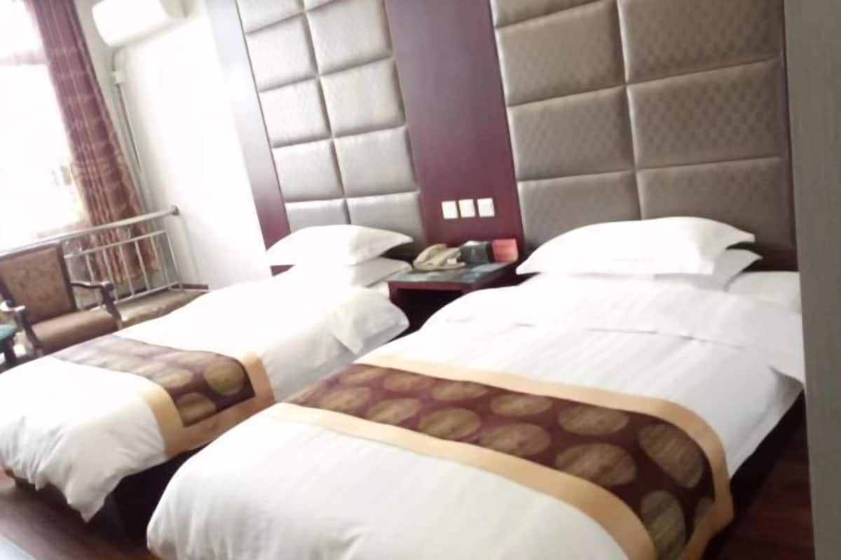 A hotel room with two beds, each with white linens and a patterned bedspread. There is a nightstand with a lamp and a telephone between the beds.