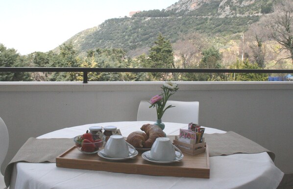 A table set with croissants, coffee cups, and a vase with flowers on a balcony overlooking a mountainous landscape. - PrimeQuerce Agriturismo (Capaccio-Paestum)