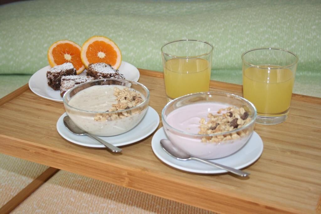 A wooden tray with two bowls of yogurt, a plate of brownies, and two glasses of orange juice.