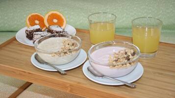 A wooden tray with two bowls of yogurt, a plate of brownies, and two glasses of orange juice.