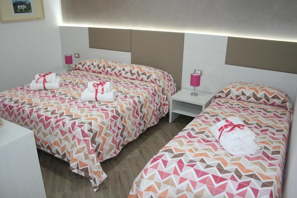 Una habitación de hotel con dos camas, cada una con una colcha estampada y una toalla enrollada. Hay lámparas de noche y una mesita entre las camas.