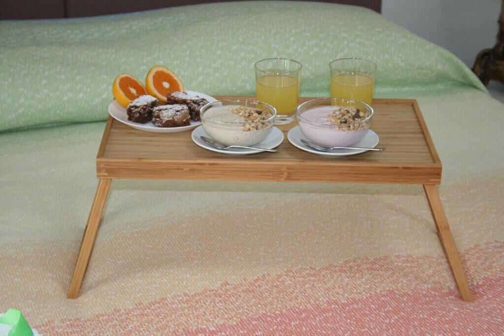 Un plateau de petit-déjeuner avec deux bols de céréales, une assiette de tranches d’orange et deux verres de jus d’orange, posé sur un lit avec un oreiller vert.