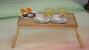 Un plateau de petit-déjeuner avec deux bols de céréales, une assiette de tranches d’orange et deux verres de jus d’orange, posé sur un lit avec un oreiller vert.