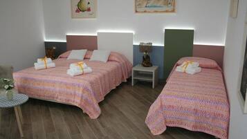 Ein Hotelzimmer mit zwei Betten, jeweils mit rosa Bettwäsche und Handtüchern. Es gibt einen kleinen Tisch mit einer Blumenvase und Kunstwerke an den Wänden.