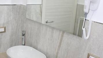 Ein Badezimmer mit einem weißen Waschbecken, einem Spiegel, einem Fön und einem Mülleimer.