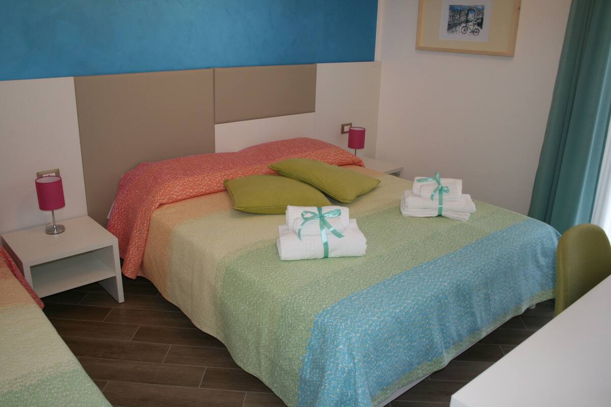 Una habitació d'hotel amb un llit, almoines, una tauleta de nit, una làmpada i un quadre al mur.