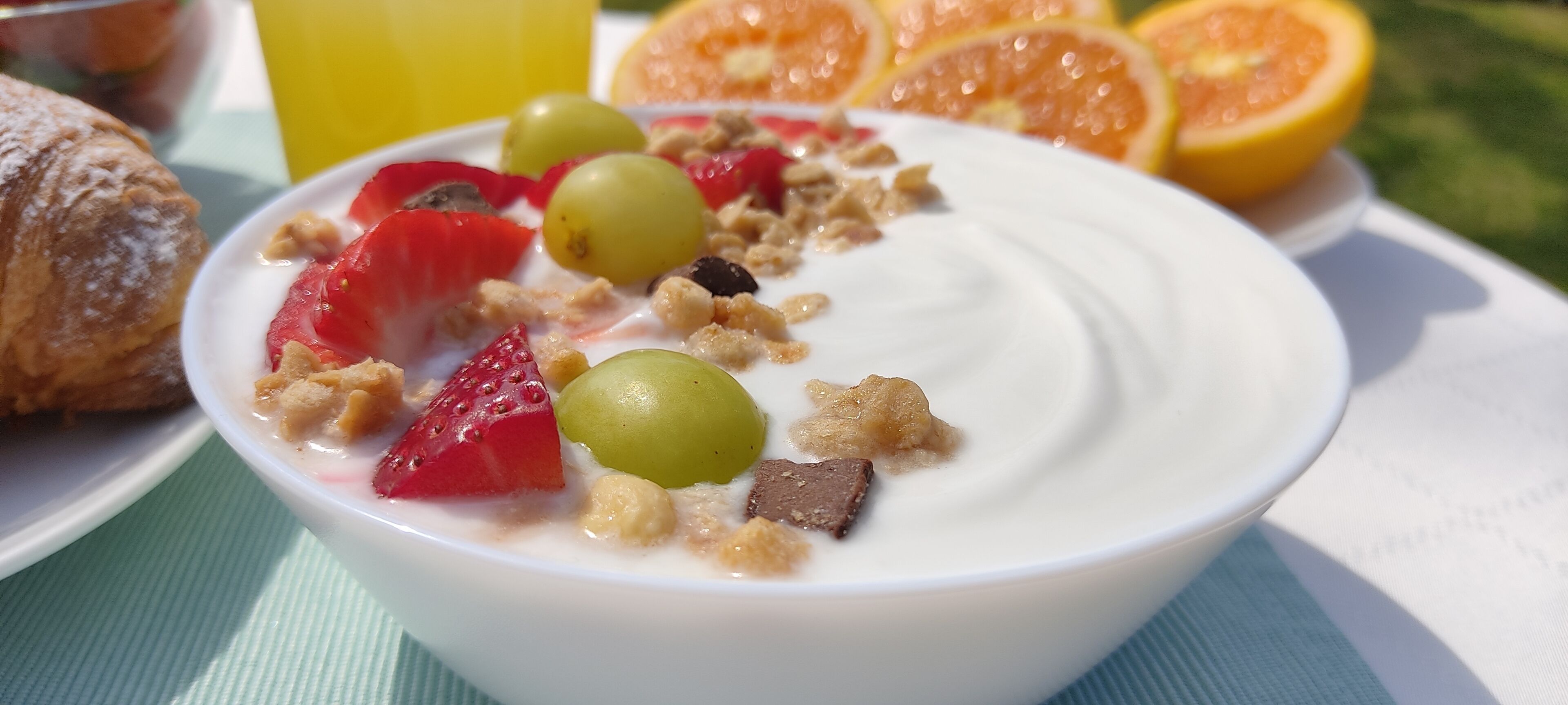 Un tazón de yogur con frutas y granola sobre un plato blanco.