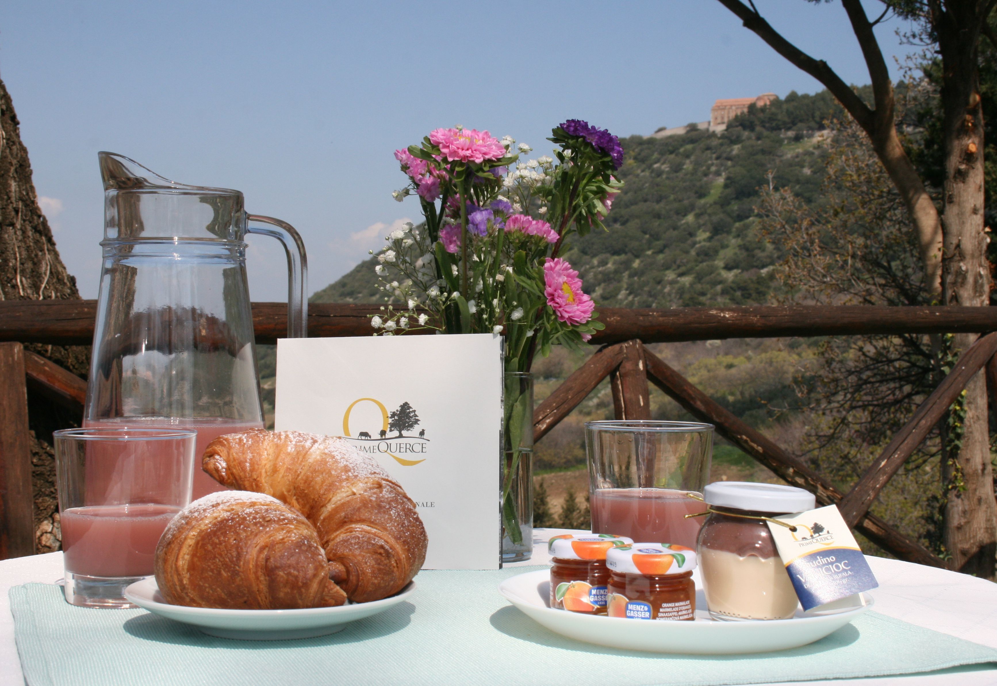 A breakfast setting with croissants, juice, and honey on a table with a scenic view.