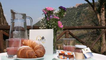 A breakfast setting with croissants, juice, and honey on a table with a scenic view.