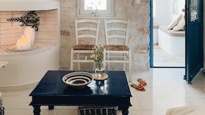 A room with a stone wall, a window, two white chairs, a table with a vase and candles, and a blue door. - Maisonette with breathtaking views of the Cyclades (Aspro Chorio)