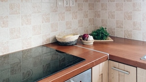 A kitchen with light wooden cabinets, a black induction cooktop, and a tiled backsplash. - Maisonette with breathtaking views of the Cyclades (Aspro Chorio)