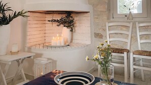 A cozy room with a white fireplace, a window with a view, and a table with a bowl and a vase. - Maisonette with breathtaking views of the Cyclades (Aspro Chorio)
