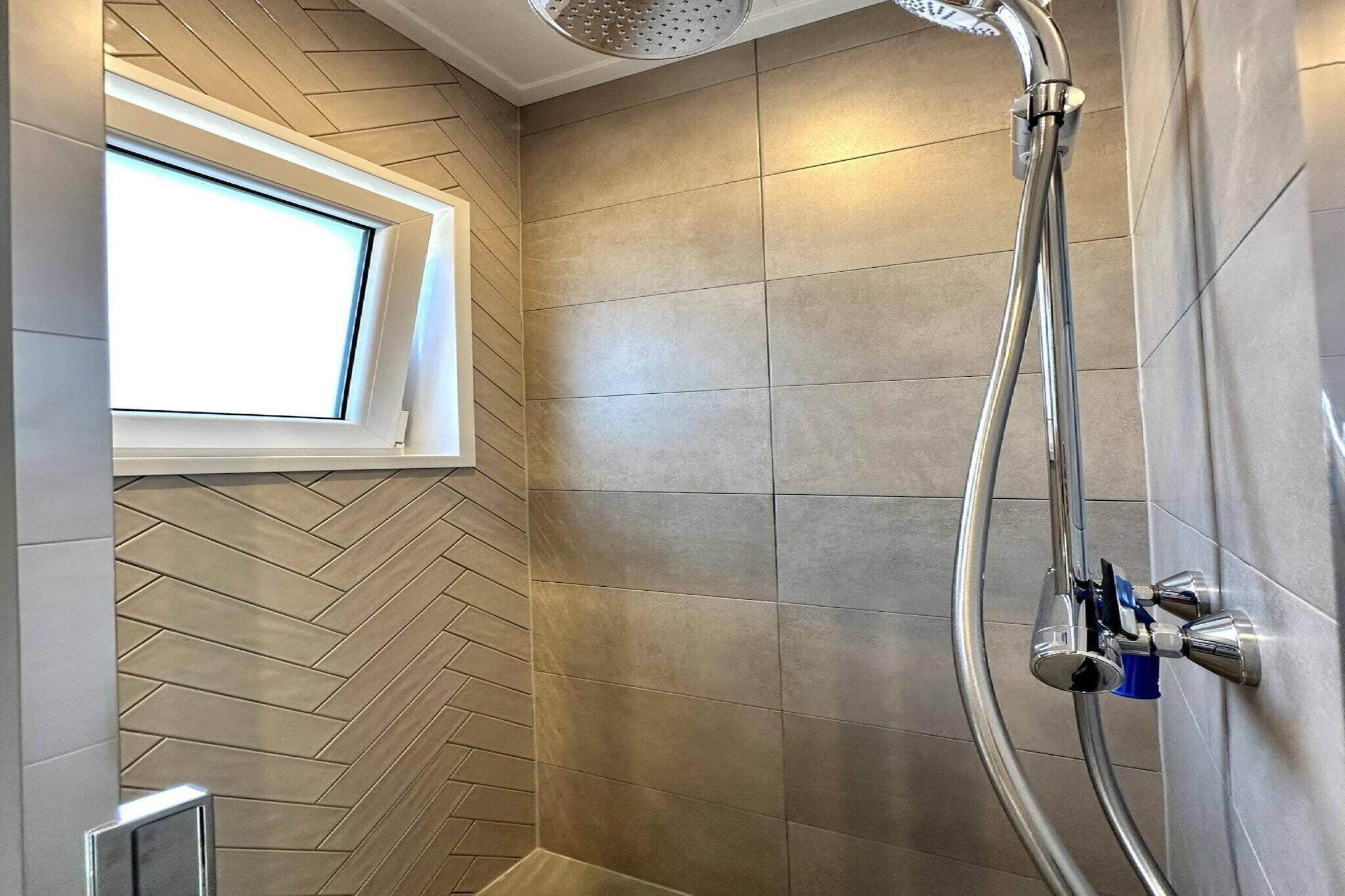 A shower with a curved hose, a window, and a herringbone-patterned wall.