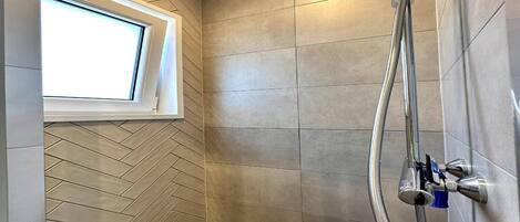 A shower with a curved hose, a window, and a herringbone-patterned wall.