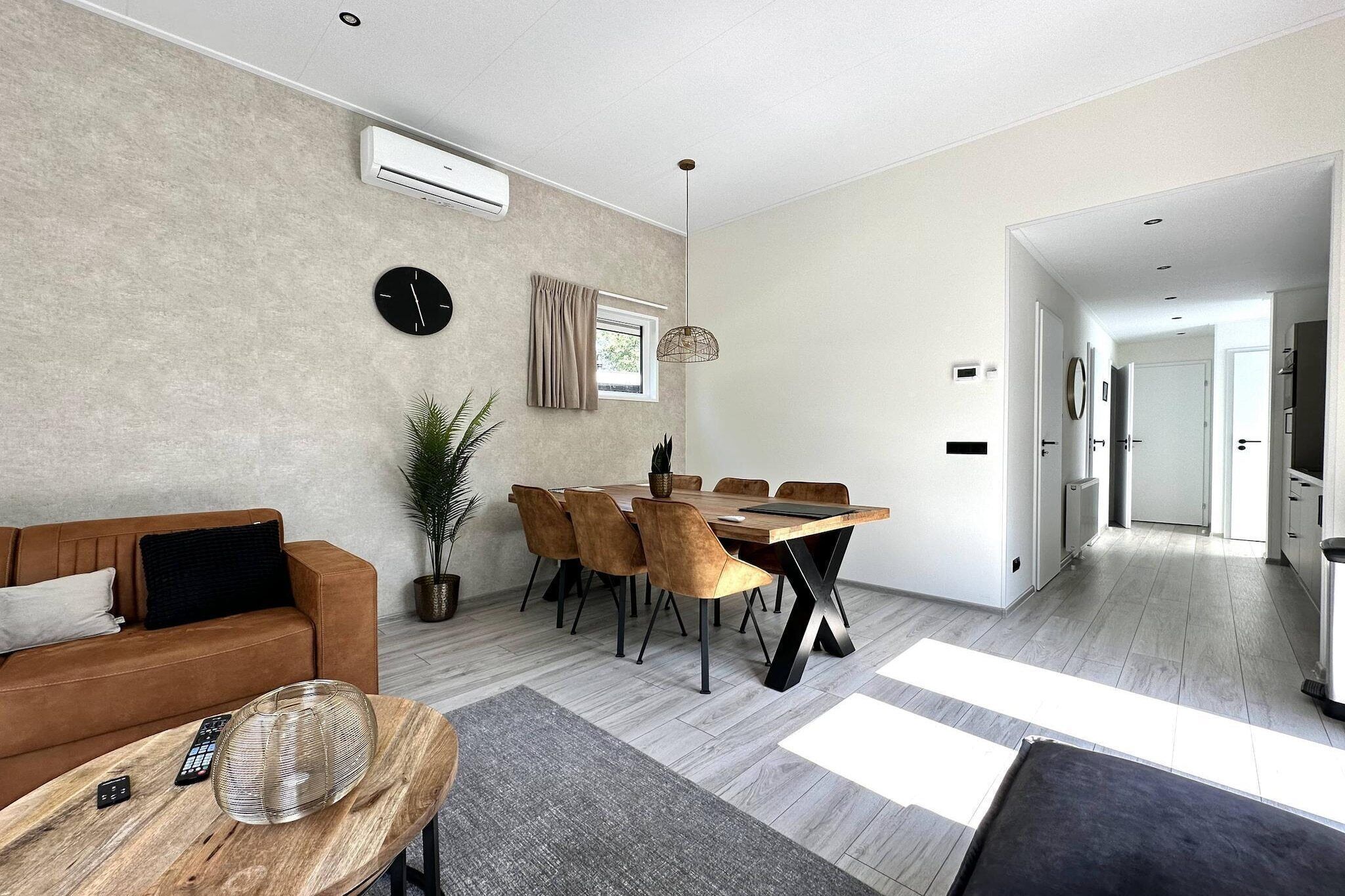 Ein modernes Wohnzimmer mit einer Couch, einem Esstisch und Stühlen. An der Wand hängt eine Uhr und über der Couch befindet sich eine Klimaanlage.