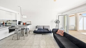 A modern kitchen with a dining area, a sofa, and a floor lamp. - Au bout de la rue la Mer T3 jardin/piscine PK/WiFi (CARQUEIRANNE)