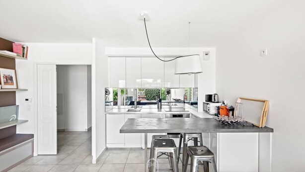 A modern kitchen with a central island, bar stools, and a view of the outdoors. - Au bout de la rue la Mer T3 jardin/piscine PK/WiFi (CARQUEIRANNE)