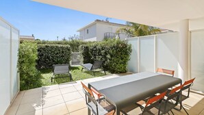 A patio area with a table and chairs, surrounded by a white wall and a hedge. - Au bout de la rue la Mer T3 jardin/piscine PK/WiFi (CARQUEIRANNE)