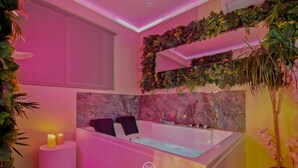 Ein modernes Badezimmer mit einer großen Badewanne, zwei Kerzen und einem an der Wand befestigten Ablagefach mit Pflanzen.