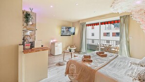 Ein Hotelzimmer mit Bett, einer kleinen Küchenzeile, einem Fernseher und einem Balkon mit Blick.