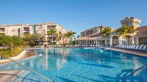 Une piscine entourée de chaises longues, de palmiers et d’immeubles à plusieurs étages dotés de balcons.