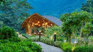 Un pavillon en bois, doté d’un toit incliné, est entouré d’une végétation luxuriante.