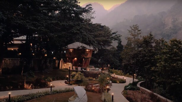 Un chalet isolé, entouré d’une forêt dense, avec un sentier sinueux menant à un bâtiment principal.