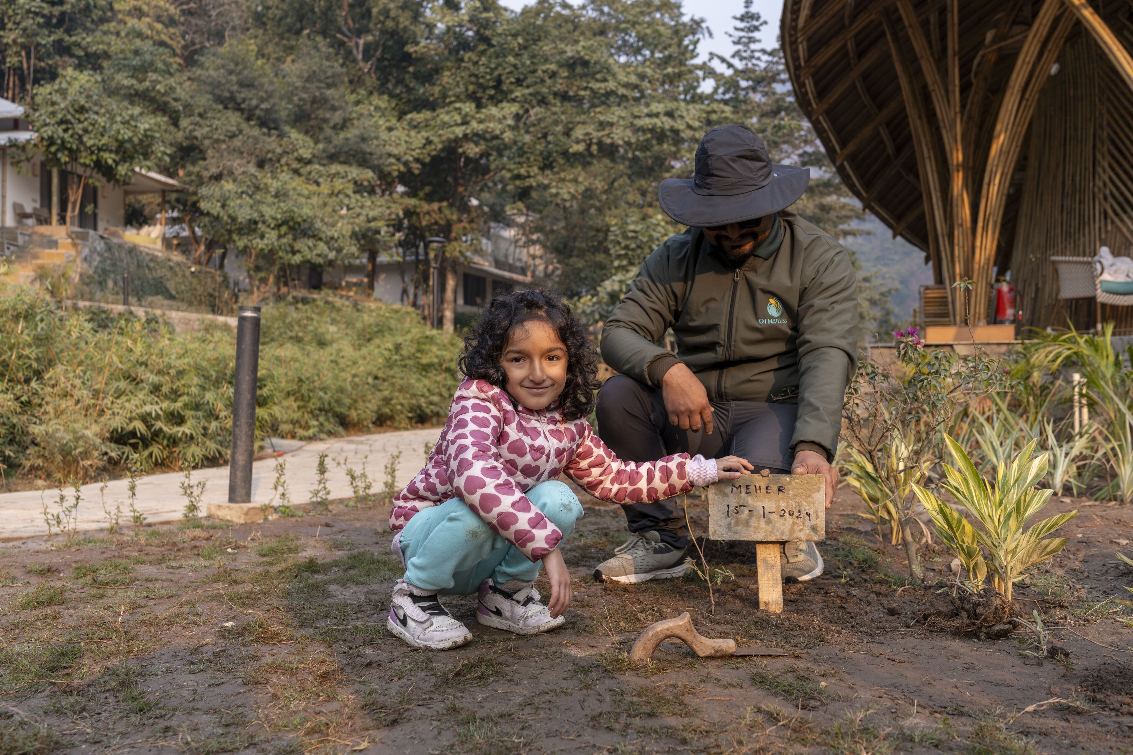 A person crouching next to a young girl holding a sign with a date.