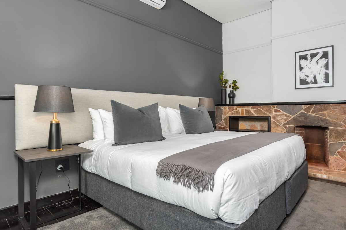 A modern bedroom with a large bed, a stone fireplace, and a nightstand with a lamp.