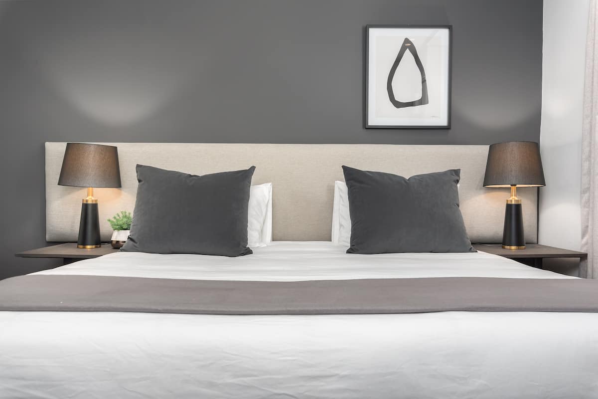 A neatly made bed with two pillows, a bedside table with a lamp, and a framed artwork on the wall.