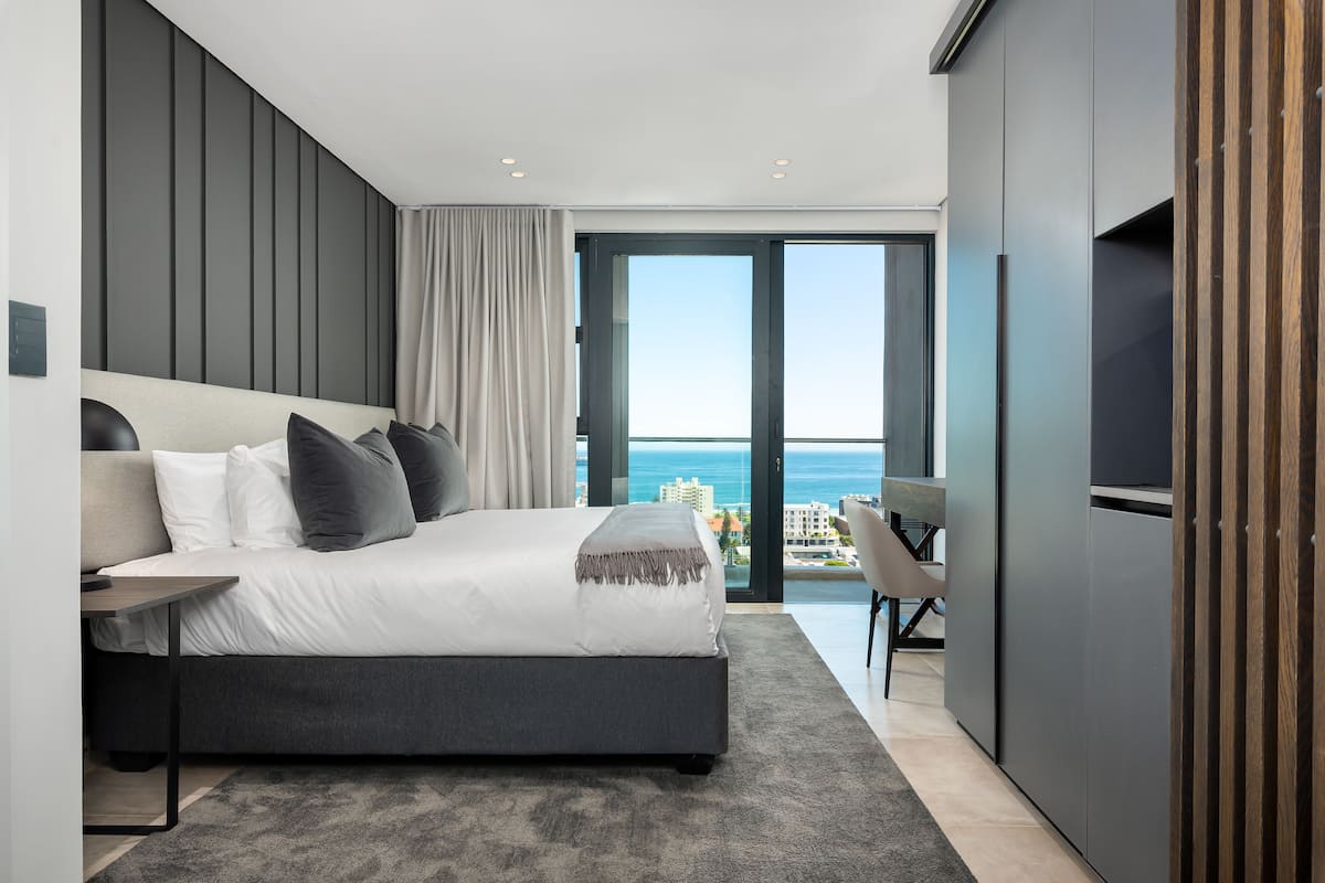 A modern bedroom with a large bed, a desk, and a view of the ocean.
